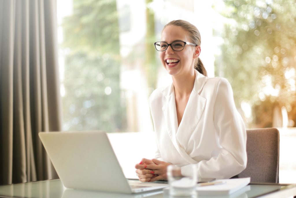 Can AI Really Replace Your Bookkeeper? Here's the Truth Small Business Owners Need Cheerful businesswoman in glasses working on a laptop, in a bright and modern office setting.